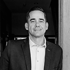 A headshot of a man wearing a blazer and a collared shirt.