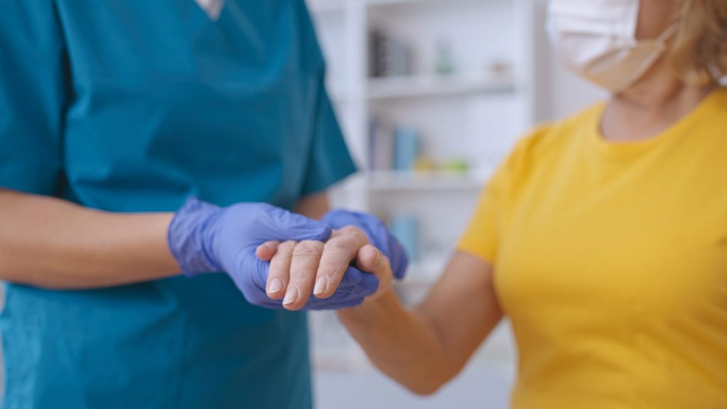 A healthcare professional in blue scrubs assessing a patient's hand.