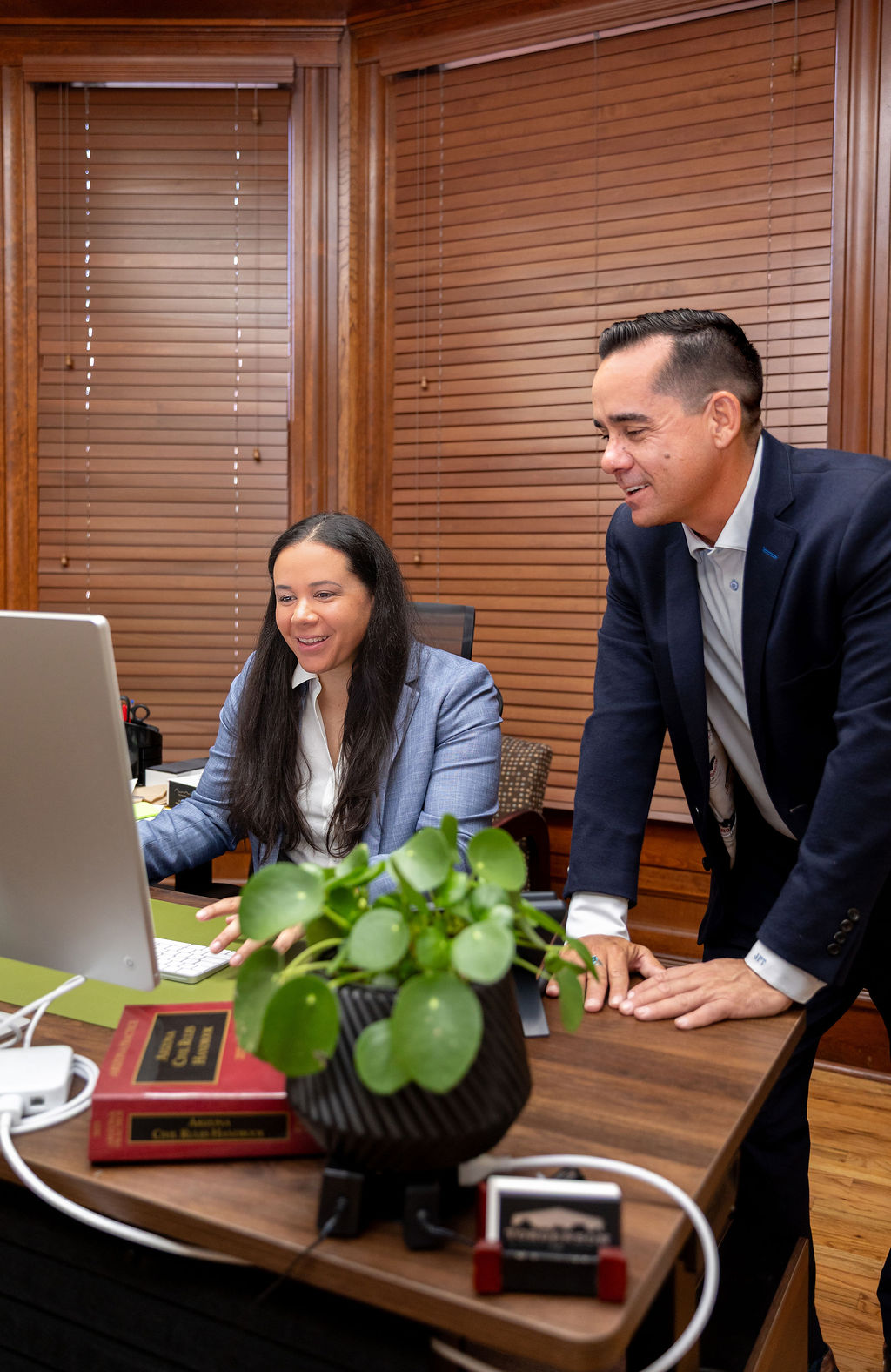 A woman and a man in business attire confer over a computer screen in an office.