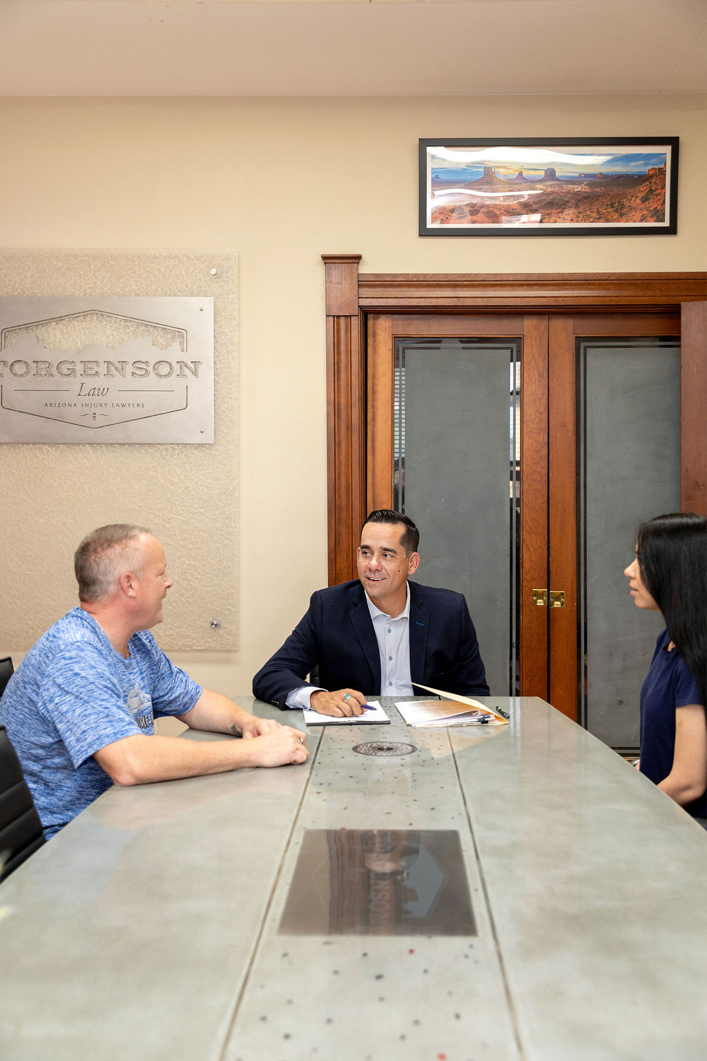 A lawyer in a suit sits at a conference table with two clients in an office.