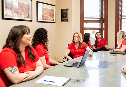 Six people wearing matching red polo shirts sit around a conference table during a meeting.