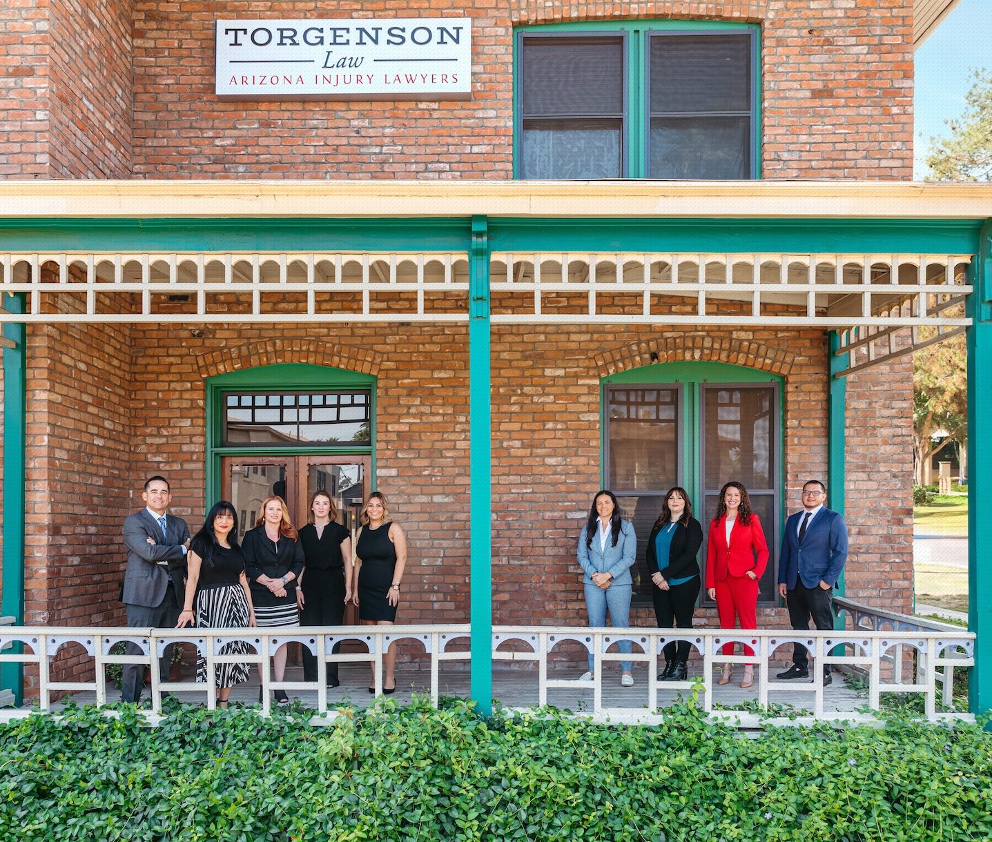 A group of nine legal professionals posing in front of a brick building with a sign that reads Torgenson Law, Arizona Injury Lawyers.