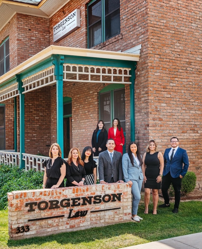A group of nine people in business attire posing in front of a brick building with a Torgenson Law sign.