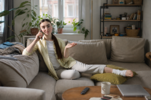 A woman sitting on a couch with a bandaged leg while talking on her phone.