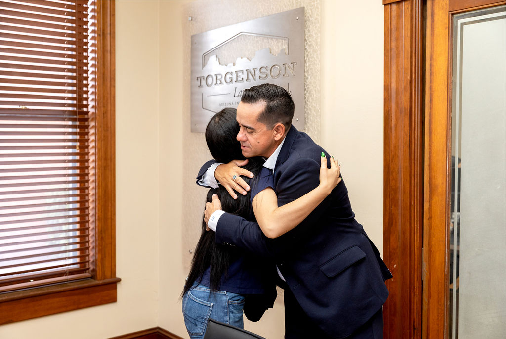 A man in a suit hugging a woman in front of a Torgenson Law office sign.