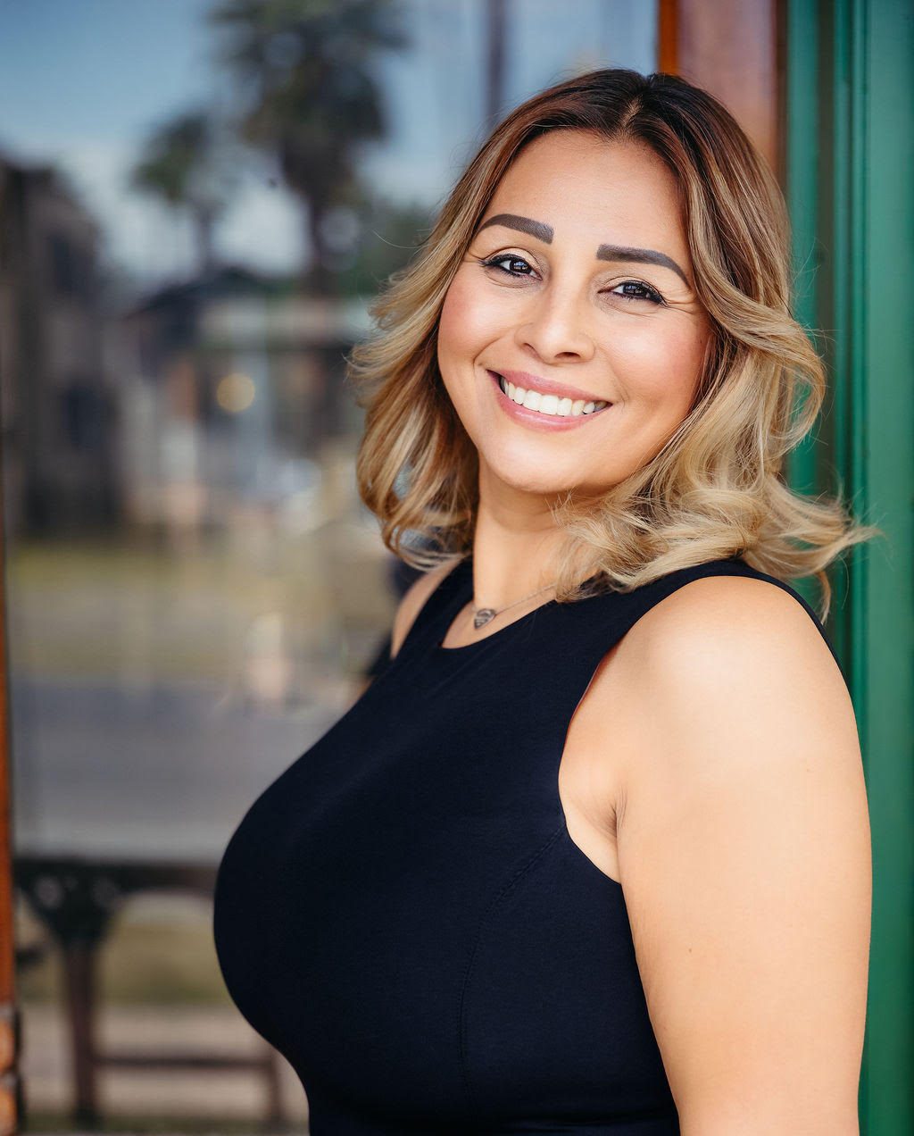 A smiling woman with shoulder-length highlighted hair wearing a black sleeveless top.