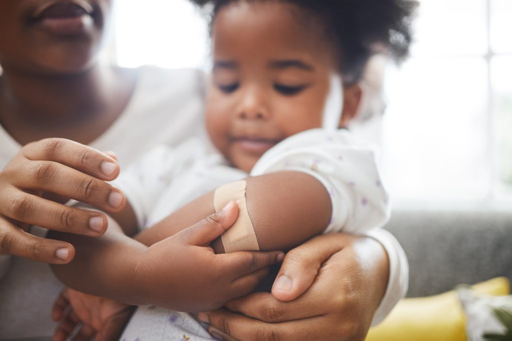 A parent holds a young child who has a bandage on their arm.